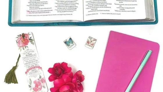 Open Bible next to a notebook, flower and bookmark