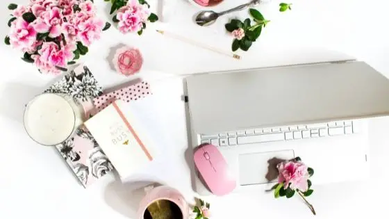 Desk with pink accessories flowers, mug and notebooks