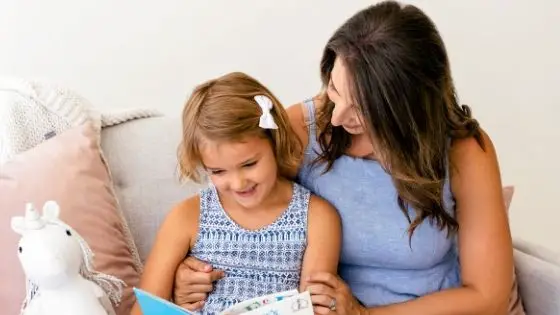 Mom and daughter sitting on couch smiling and reading together