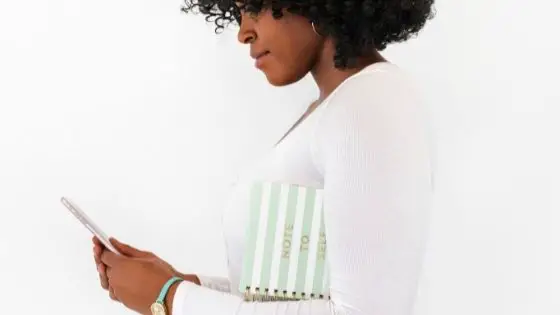 African-American woman holding phone with notebook under her arms
