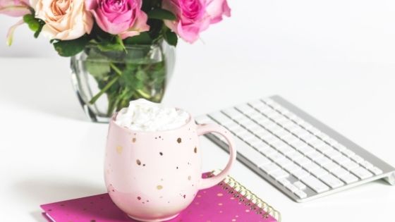 Mug on pink notebook next to flowers and computer keyboard