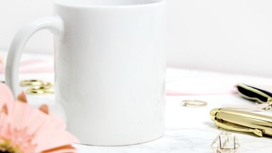 White mug next to gold pen and pink flower
