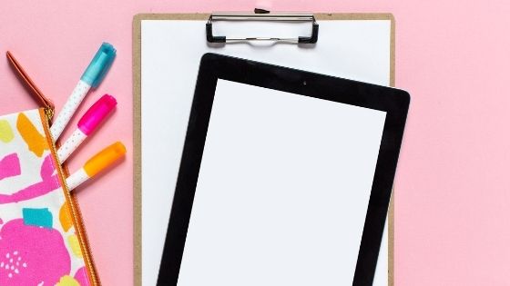 Colorful pens coming out of a pencil case next to a tablet and list board