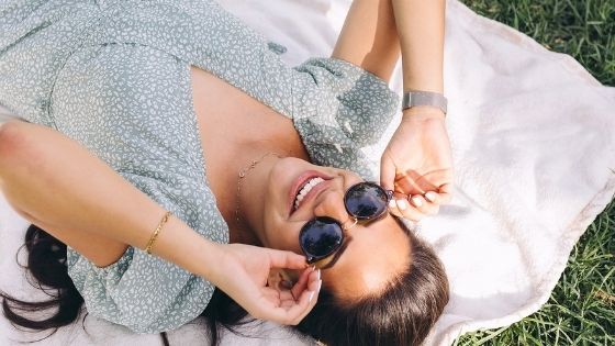 Caucasian girl with sunglasses smiling while looking up and lying on the grass