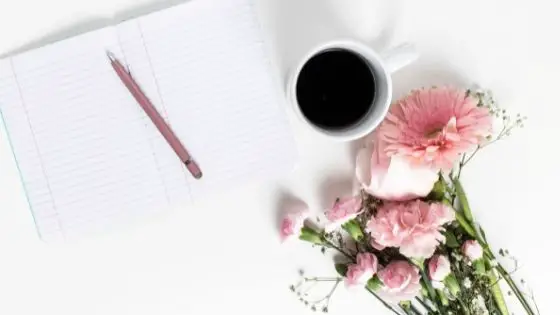Open notebook with pen next to a cup of coffee and pink flowers