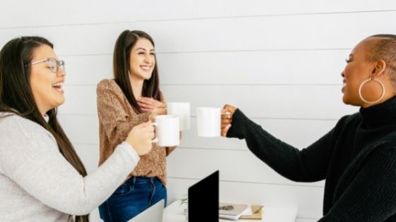 Black American and white women smiling and making a toast with coffee mugs