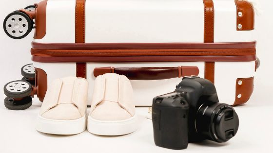 Closed suitcase on the floor with a camera and shoes next to it