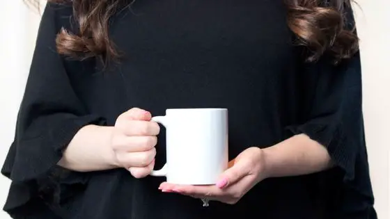 Caucasian woman wearing black and holding a cup of coffee