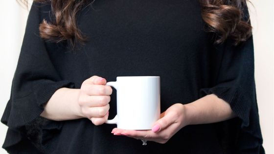 Caucasian woman wearing black and holding a cup of coffee