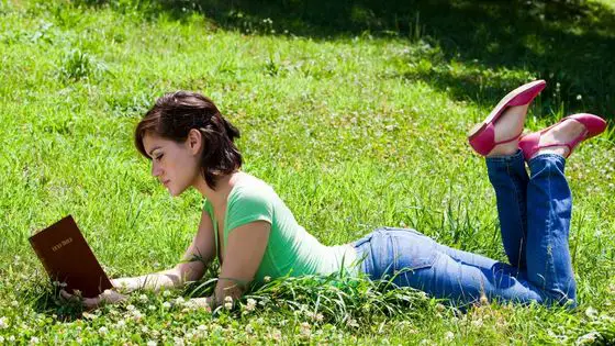 Young Caucasian woman lying on the grass reading her Bible