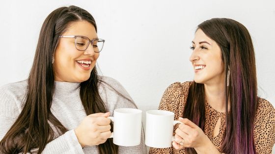 Two Caucasian women laughing and holding cups of coffee